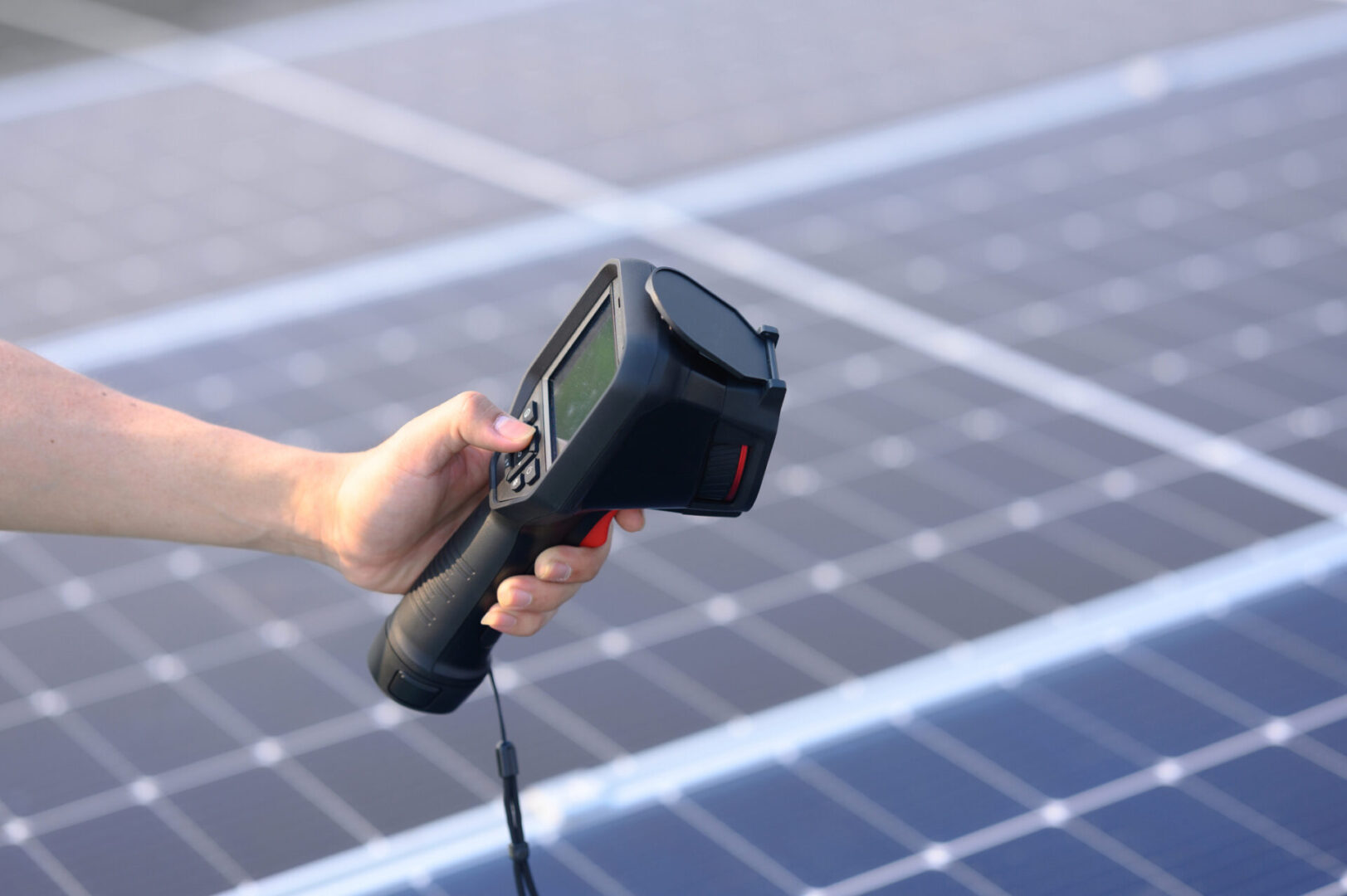 Hand holding a thermal camera over solar panels.